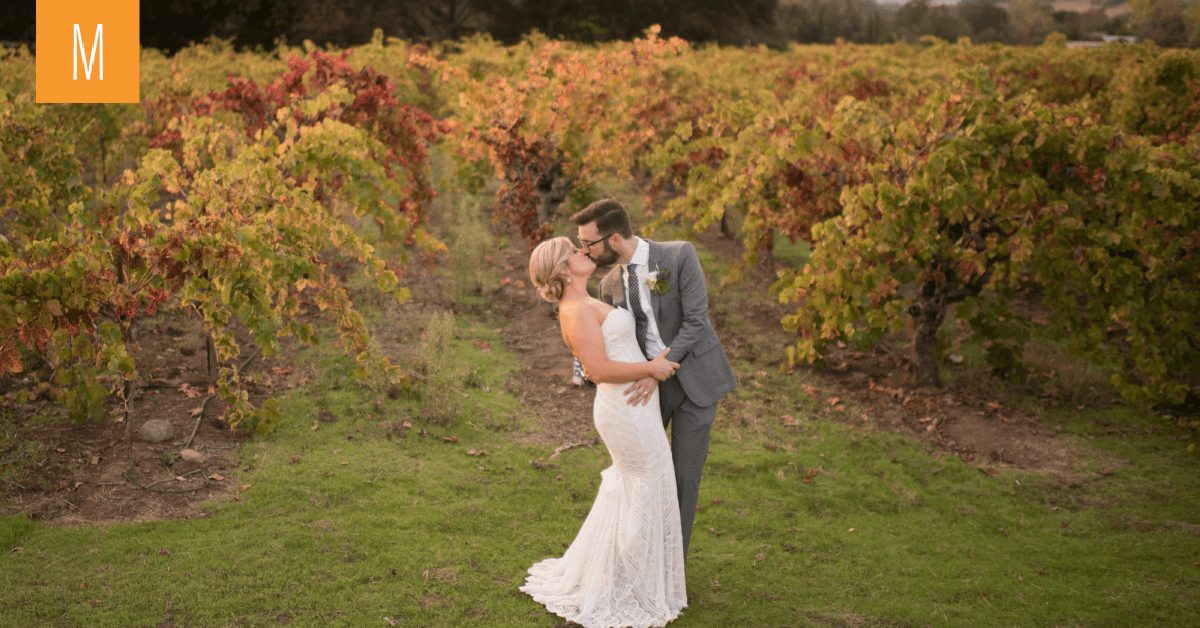 Romantic photo of a bride and groom kissing in front of fall turned grape vines.
