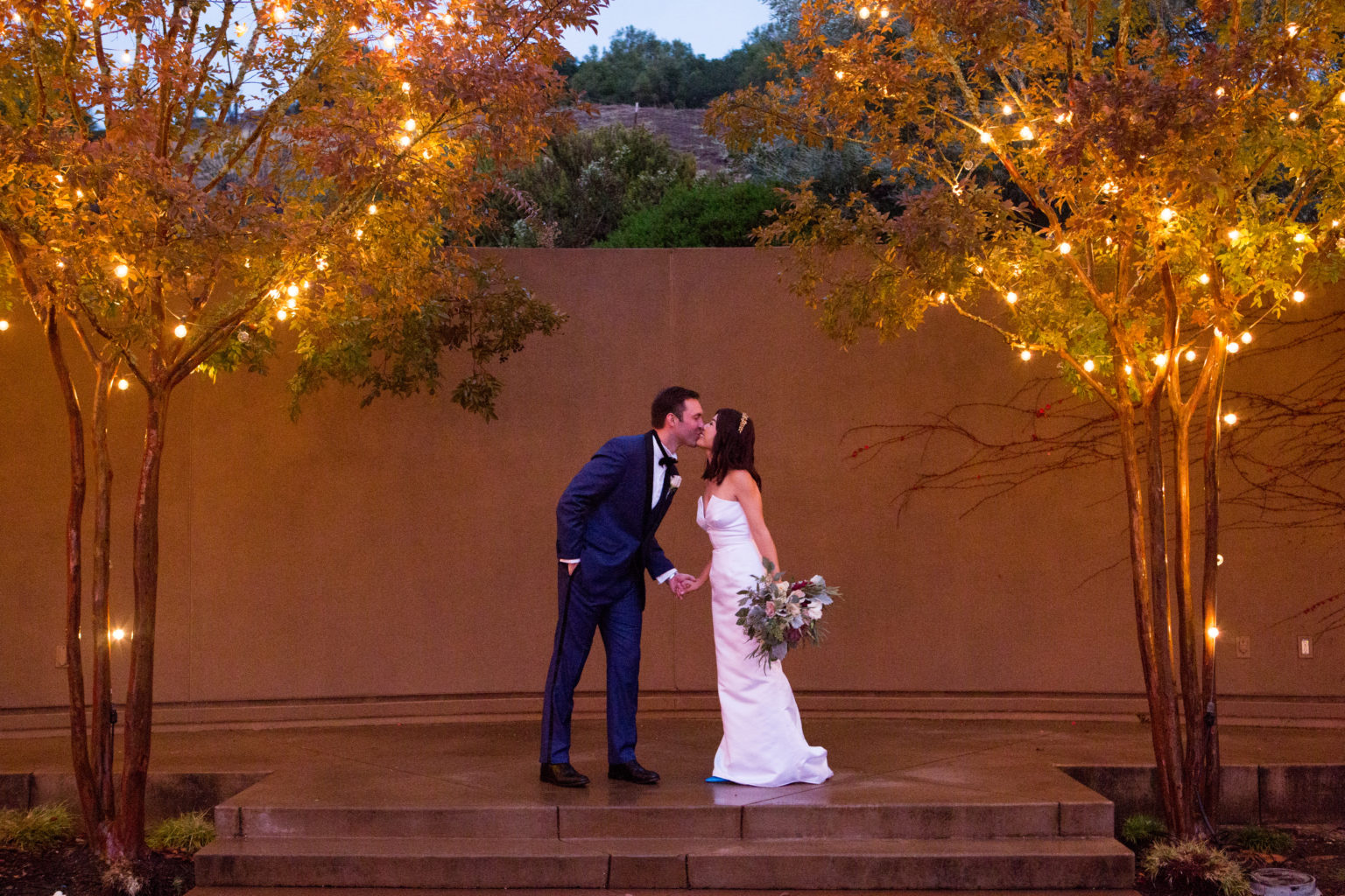 Wedding couple kissing between lighted trees at Paradise Ridge winery