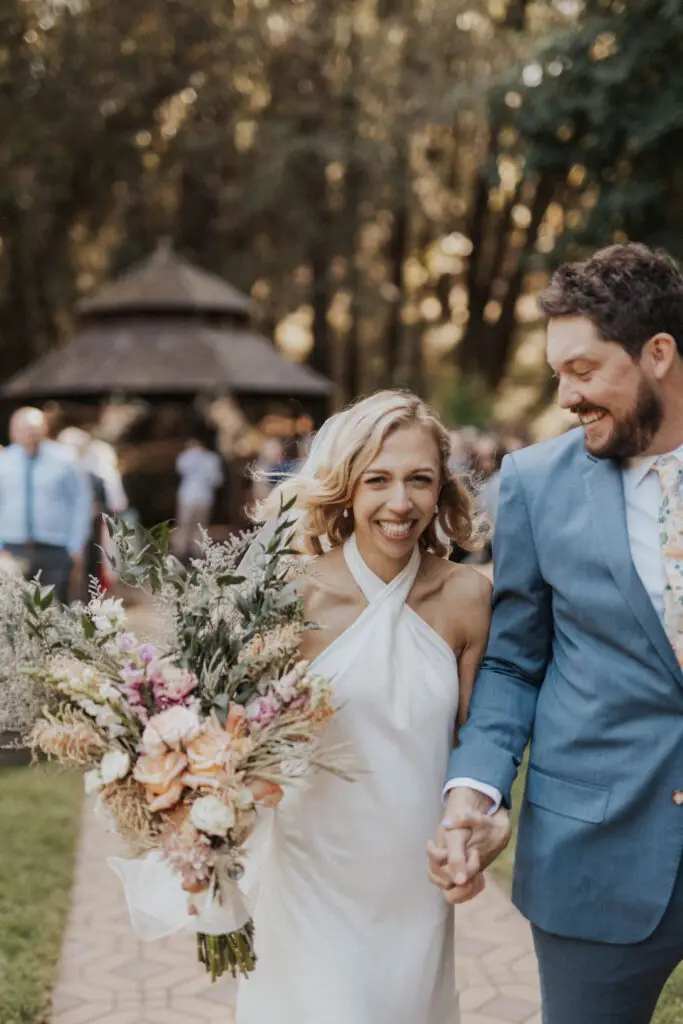 Woman with bouquet holds hand with man smiling.