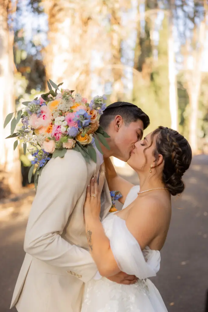 Bride with colorful bouquet kisses groom.